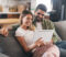 Young adult couple siting on sofa. Women is holding tablet, they are both watching something and laughing