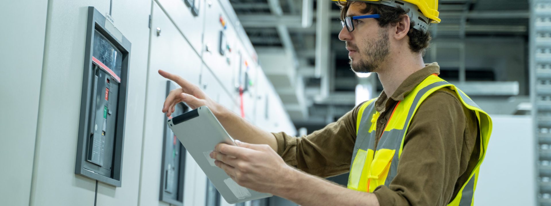 Electrical engineer working on the tablet and recording the voltage current and power of electrical power distribution board in switch gear room